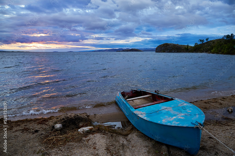An old boat by the lake shore. Beautiful sunrise over the water, stormy sky. 