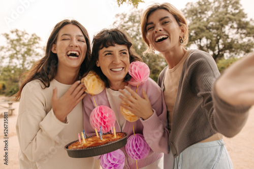 Funny european young girls with cake are laughing spending holiday outdoors together. Brunettes, blonde wear casual spring clothes. Lifestyle concept