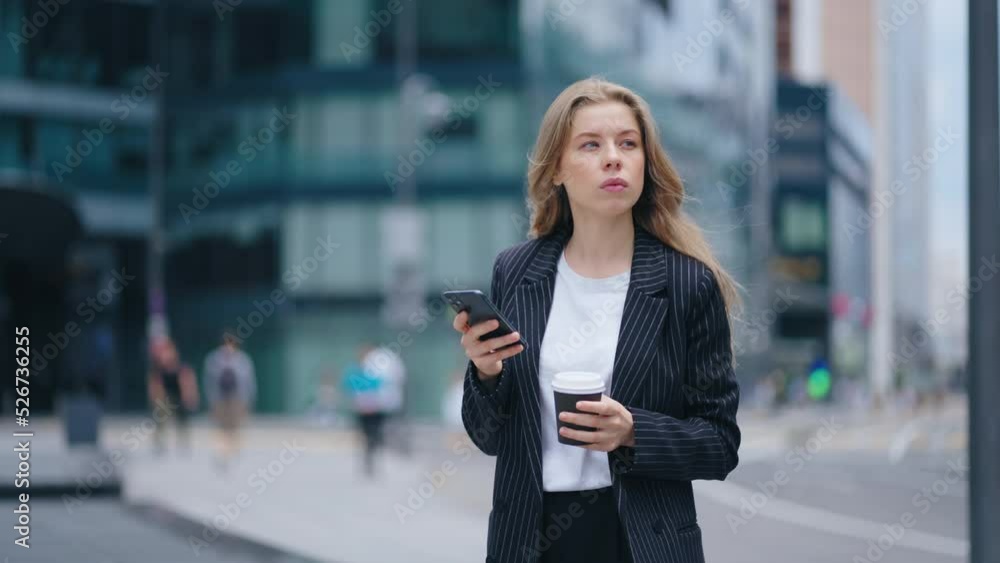 beautiful blonde woman in business suit is reading news in smartphone, standing on city street beautiful blonde woman in business suit is reading news in smartphone, standing on city street