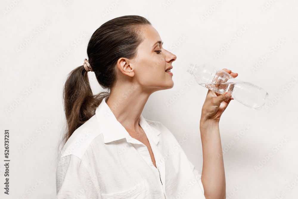 Young happy caucasian woman in white shirt drinks water from a bottle, copyspace Young happy caucasian woman in white shirt drinks water from a bottle, copyspace