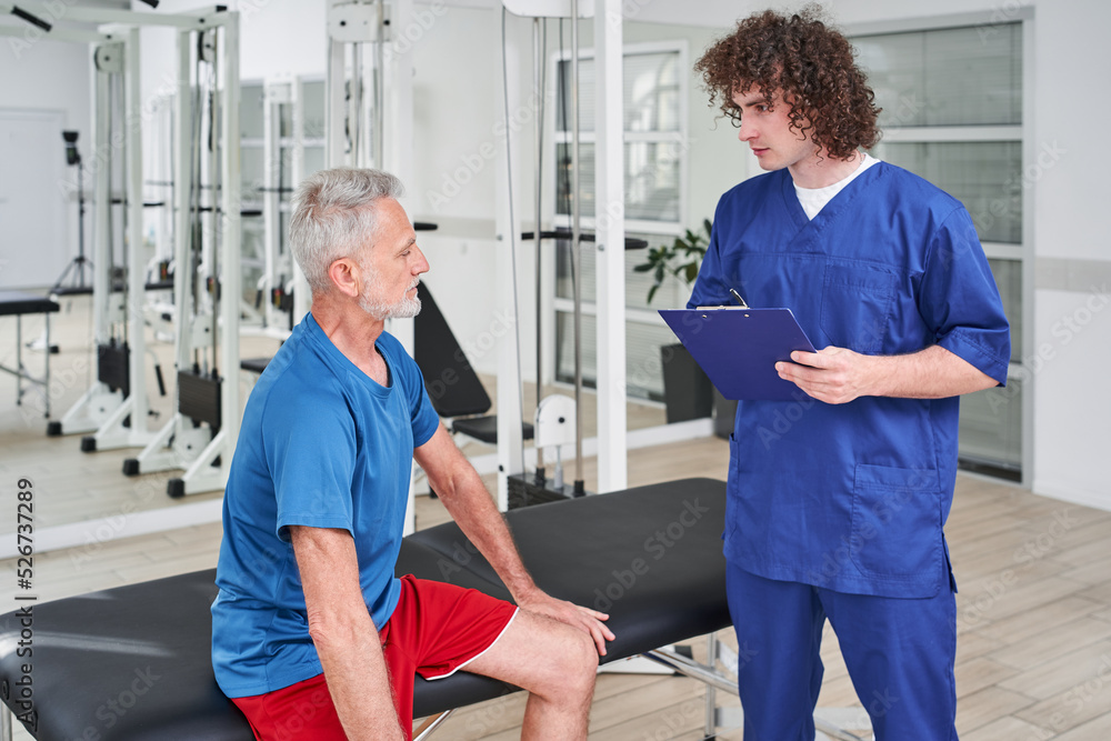 Obraz premium Male manual therapist telling prescriptions to his male patient at rehabilitation centre