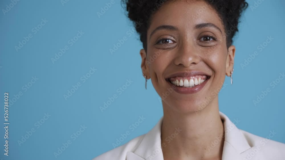 Face of happy hispanic curly haired woman wearing white jacket looking at the camera in the blue studio Face of happy hispanic curly haired woman wearing white jacket looking at the camera in the blue studio