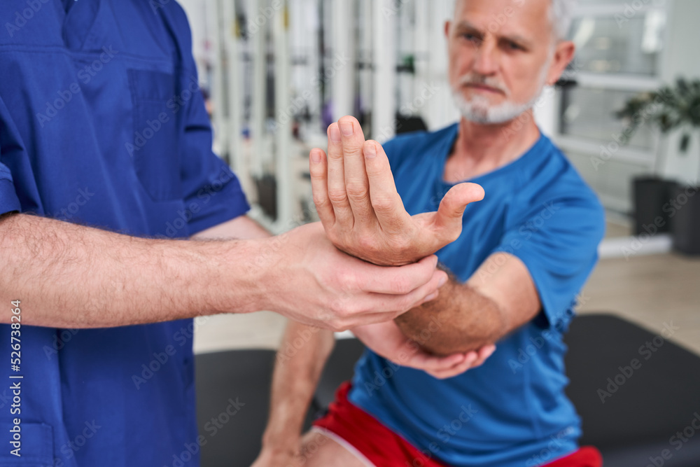 Obraz premium Senior man receiving massage by male physic therapist of his arm due to injury