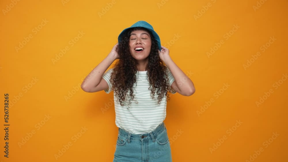 Surprised brunette curly haired woman wearing panama hat rejoicing at the camera in the yellow studio Surprised brunette curly haired woman wearing panama hat rejoicing at the camera in the yellow studio