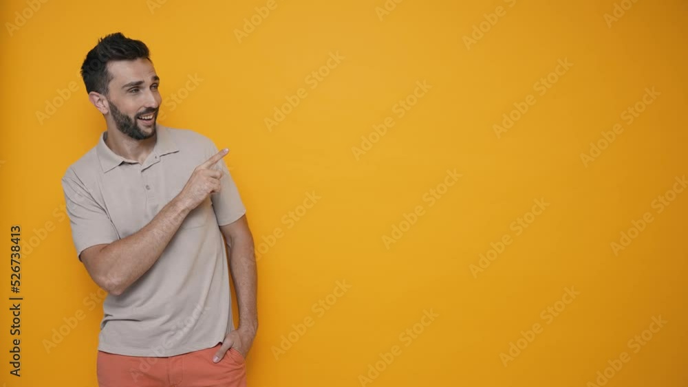 Smiling brunet man wearing t-shirt pointing fingers to the copyspace and looking at the camera in the yellow studio Smiling brunet man wearing t-shirt pointing fingers to the copyspace and looking at the camera in the yellow studio
