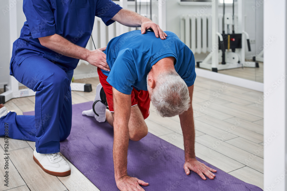 Elderly man stretching rehab physio band with young physiotherapist during the treatment