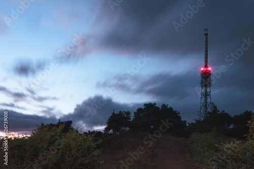 Radio tower with red light at night surrounded by trees and clouds