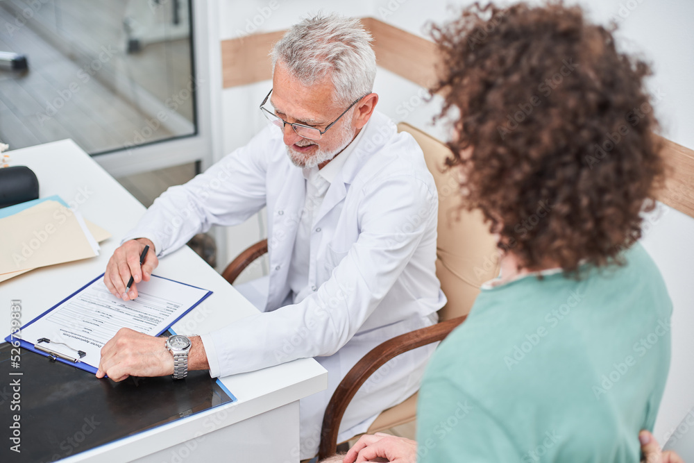 Obraz premium Cheerful doctor and patient sitting opposite each other and talking while discussing symptoms