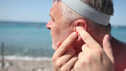 Mature man putting silicone ear plugs, surfers earplugs, swim plugs