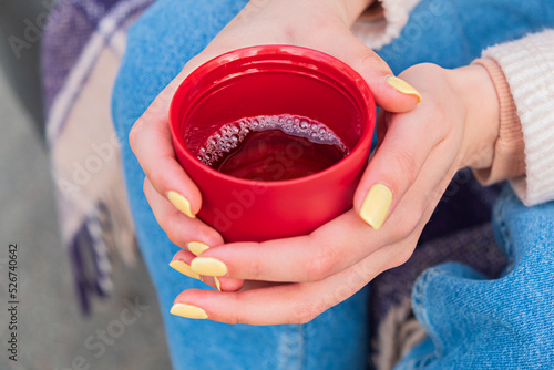 Close-up of a red cup of tea in women's hands with yellow nail polish
