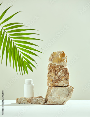 Podium of marble stones with mockup plastic jar, green palm leaf. Presentation of natural dietary supplement, vitamins