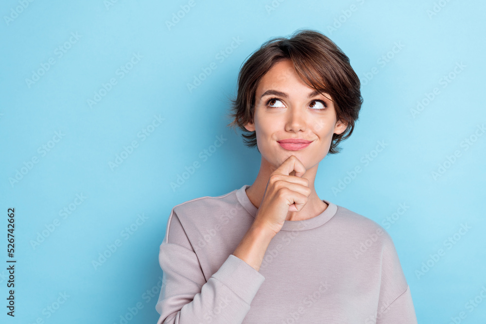 Portrait of cute positive girl bob hairdo dressed gray sweatshirt hold hand on chin look empty space isolated on blue color background Portrait of cute positive girl bob hairdo dressed gray sweatshirt hold hand on chin look empty space isolated on blue color background