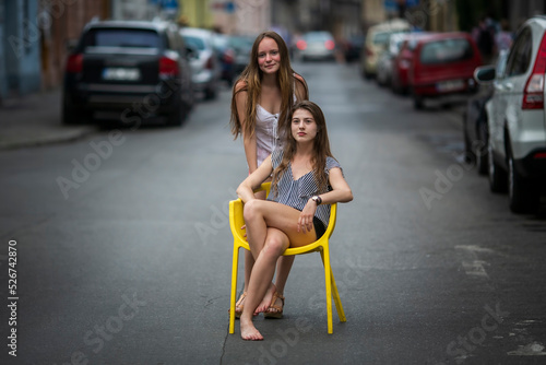 Two cute teengirls girlfriends pose in the middle of the street in old town.