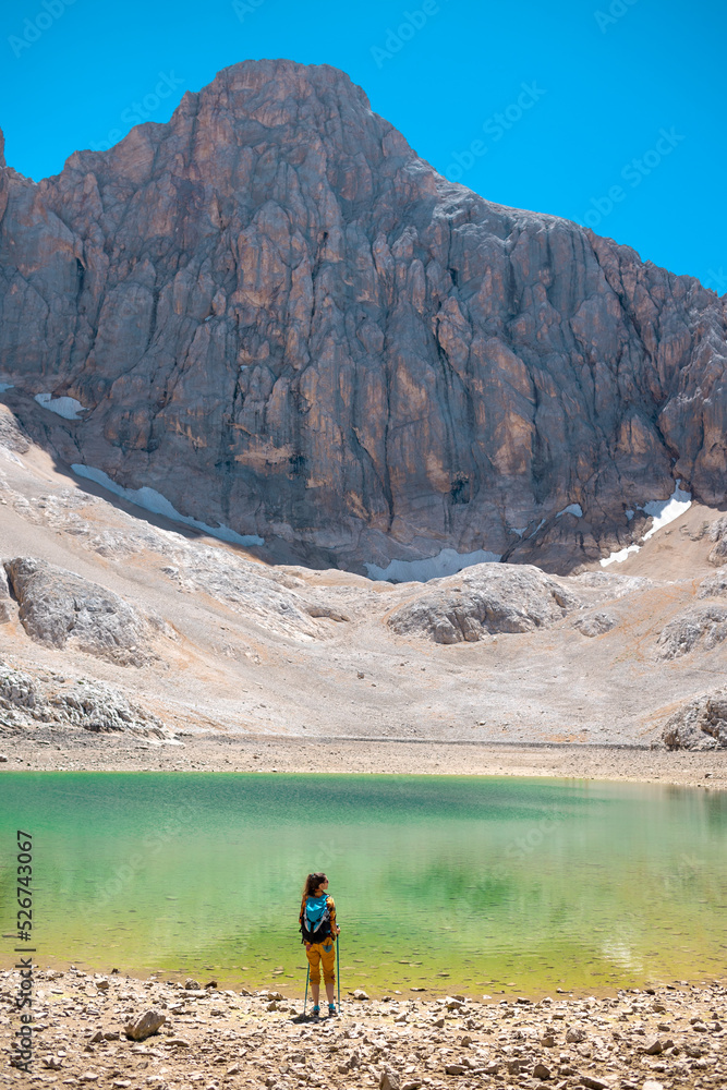 A woman with a backpack stands against the backdrop of a lake and mountains.