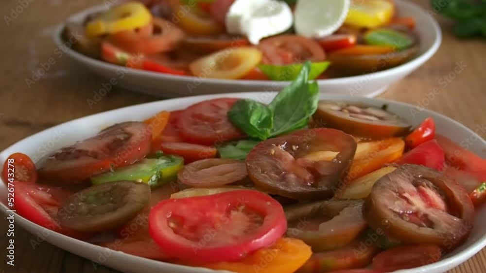 Woman adding slices of mozzarella cheese to several plates of tomatoes, preparing an italian meal recipe (caprese salad) Woman adding slices of mozzarella cheese to several plates of tomatoes, preparing an italian meal recipe (caprese salad)