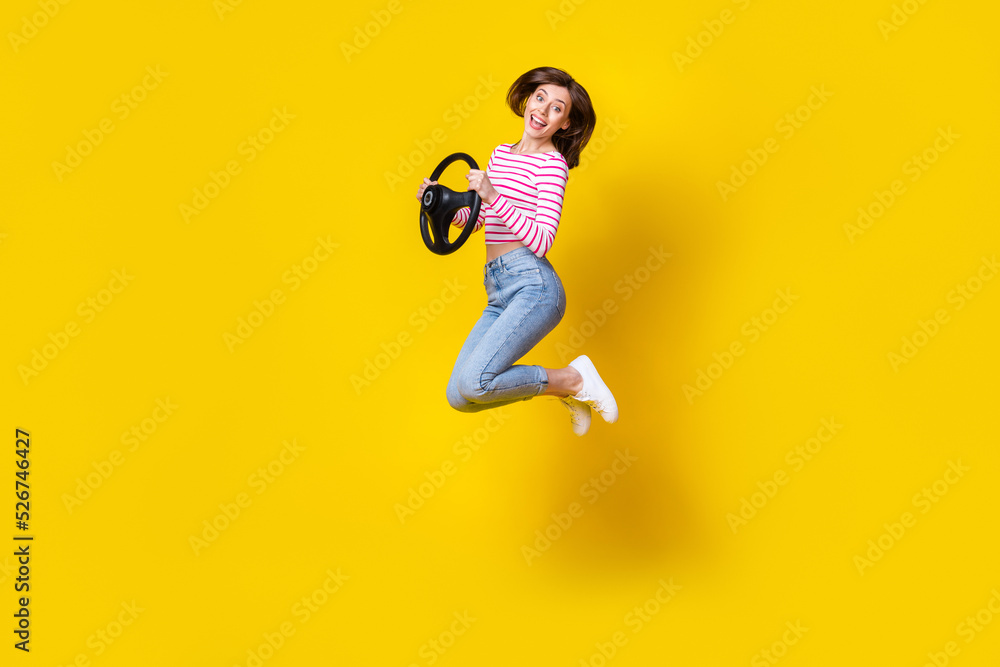 Full length photo of cute gorgeous impressed girl brunette hair wear jeans jumping hold steering wheel isolated on yellow color background