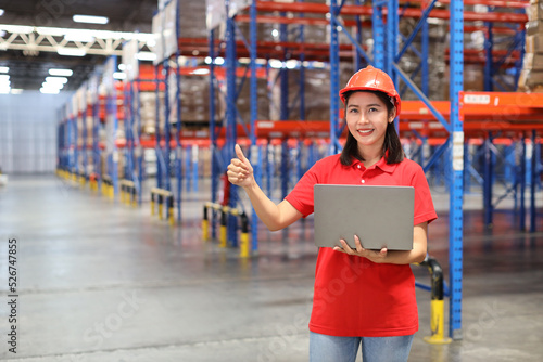 Portrait of warehouse workers young asian woman standing and using computer while showing thumb up and controlling stock and inventory in retail warehouse logistics, distribution center