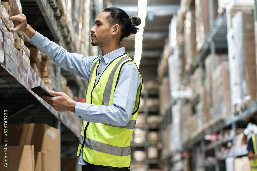 Fototapeta premium Asian male worker carries a tablet to count furniture items check box inspecting bracode before sending it to customers in a furniture wholesale warehouse.