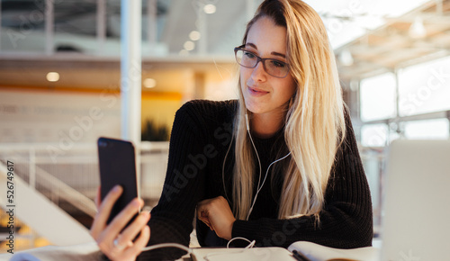 Young blonde caucasian female making a video call from her mobile phone while studying in university library