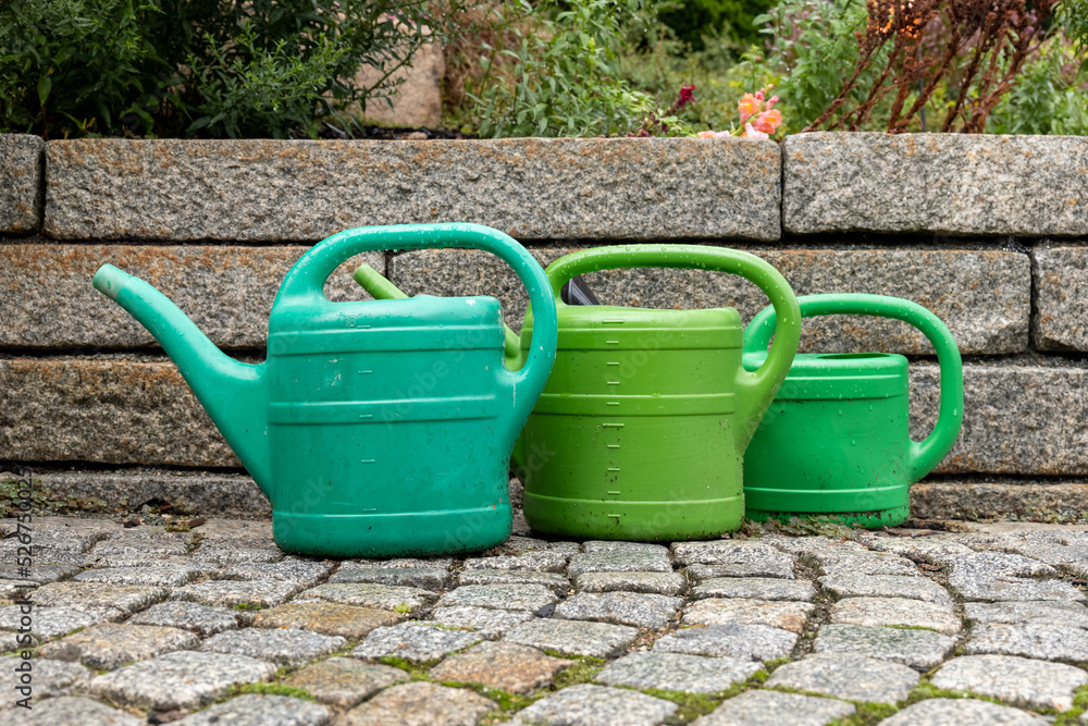 three watering cans in front of a small wall three watering cans in front of a small wall