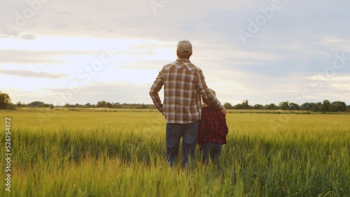 Farmer and his son in front of a sunset agricultural landscape. Man and a boy in a countryside field. Fatherhood, country life, farming and country lifestyle. © Acronym