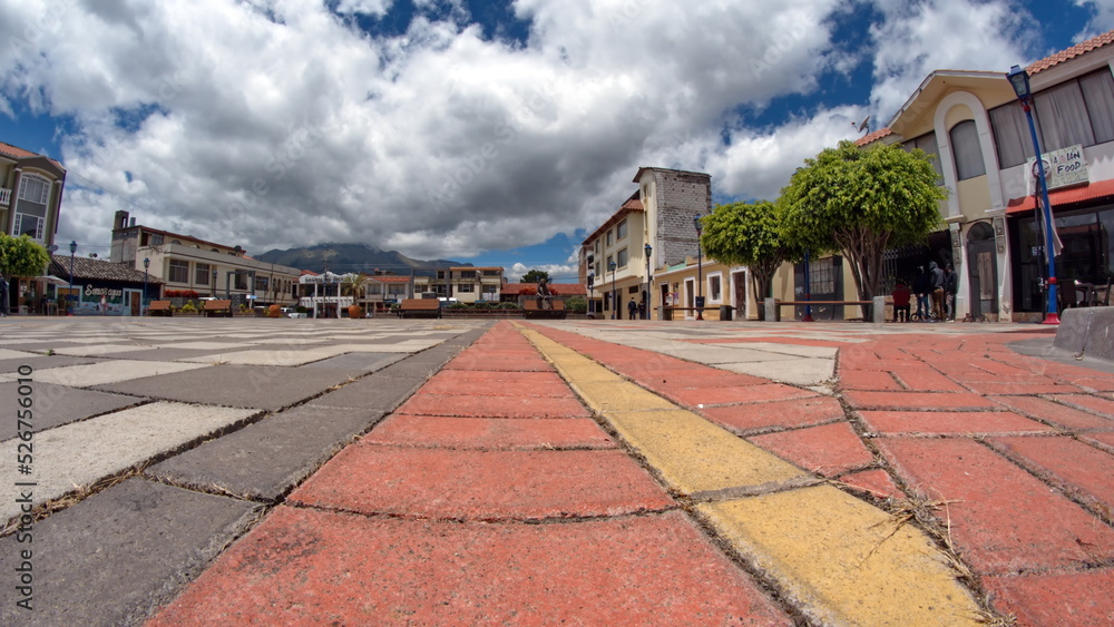 Tiles forming lines and checkerboard patterns on the ground in Ornamental Park in Cotacachi, Ecuador, taken with a fisheye lens, with a blue sky and white clouds above