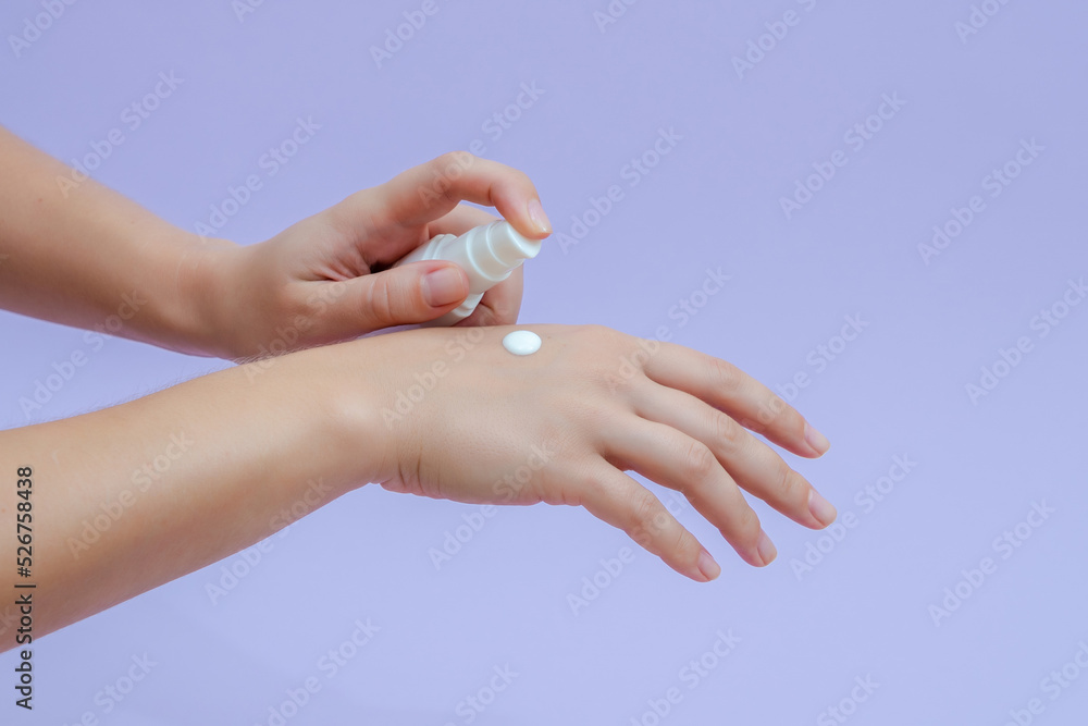 Woman's hand squeezing out cream in white tube isolated on lilac background. Beauty concept. Tube for cosmetic products Woman's hand squeezing out cream in white tube isolated on lilac background. Beauty concept. Tube for cosmetic products