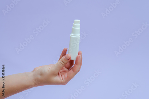 Womans hand holds a white tube (cream battle) for cosmetic products isolated on lilac background. Beauty concept