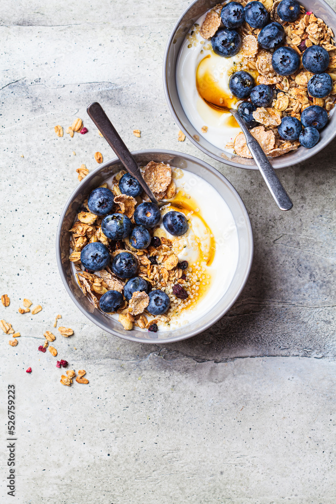 Breakfast yogurt bowl with granola, blueberries and maple syrup, gray background. Breakfast yogurt bowl with granola, blueberries and maple syrup, gray background.