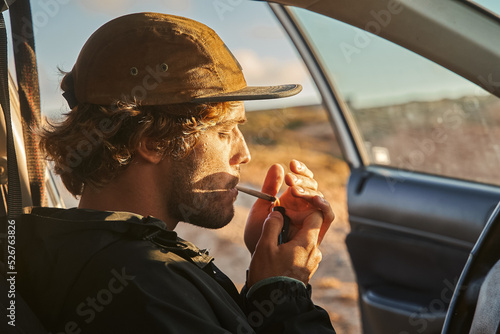 Concentrated man lighting hand rolled cigarette while smoking tobacco at his car photo