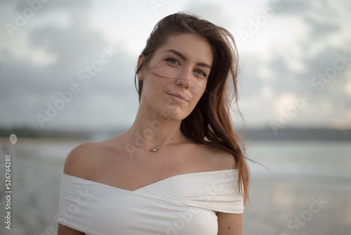 Portrait of young woman at ocean side looking at camera. Smiling female standing at the beach.