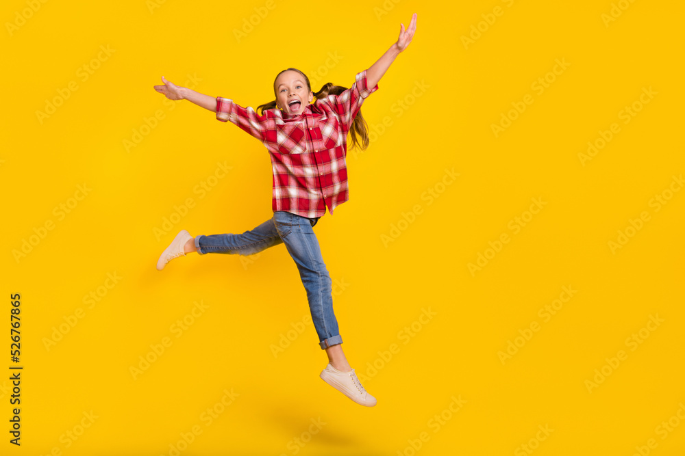 Photo of excited pretty schoolgirl wear checkered shirt jumping high walking empty space isolated yellow color background