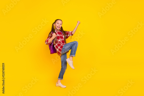 Photo of sweet funky schoolgirl wear checkered shirt walking rising fists isolated yellow color background
