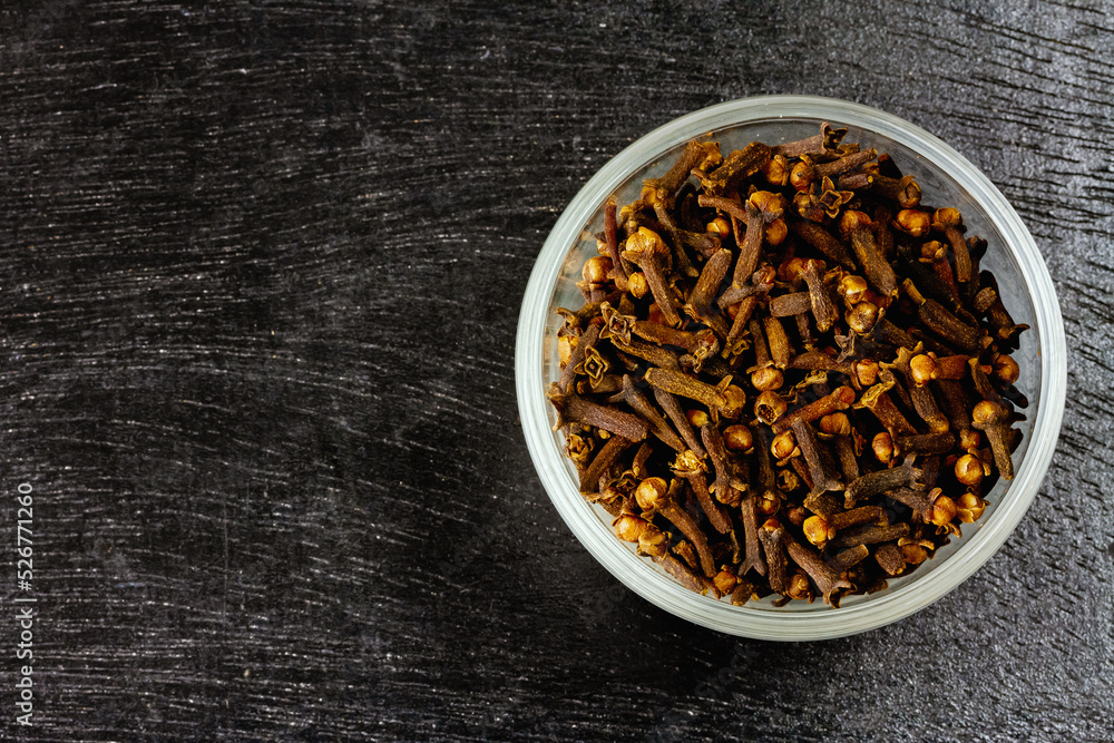 Cloves in glass bowl on black wooden background, top view, copy space. Herbal cloves have a fragrant and spicy flavor. Cloves in glass bowl on black wooden background, top view, copy space. Herbal cloves have a fragrant and spicy flavor.