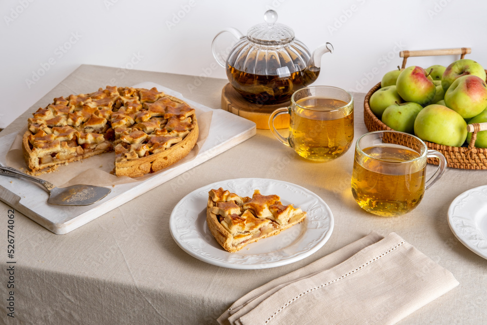 Homemade apple pie on cutting board and glass teapot with cups on a family table. Autumn baking