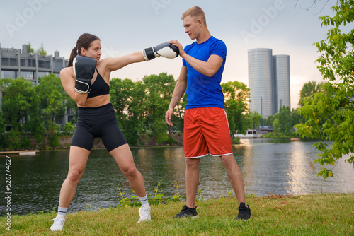 Fototapeta Naklejka Na Ścianę i Meble -  Shot of young female boxer working out with her personal trainer outdoors in summertime.