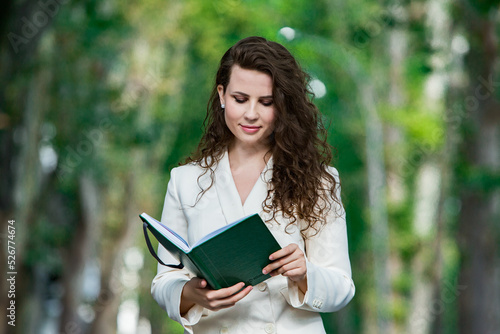 The portrait of a business woman with a notebook in her hand. Smartly dressed girl outside. Successful white european woman.