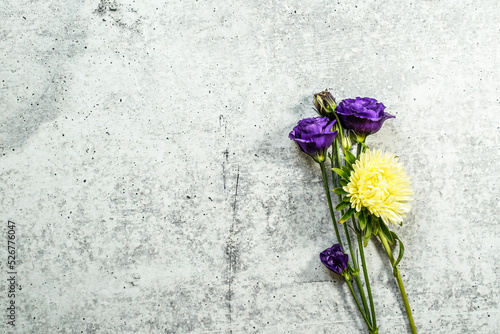Purple lisianthus flowers and a single yellow aster flower placed at the right of the image allowing for text at the left.  Concrete background.
