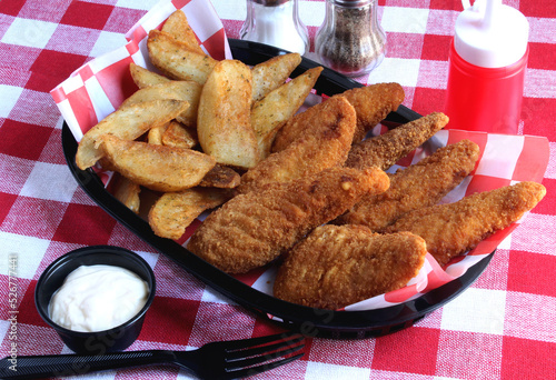 Potato wedges and chicken tenders in a black deli basket.