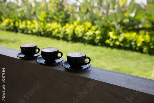 Three Cups of hot cappuccino on concrete bar table with green sunny background