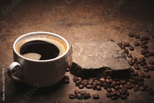 Cup of freshly brewed roasted coffee beans on brown background
