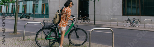 Photography amazed young woman in summer outfit riding bicycle on street in berlin, banner