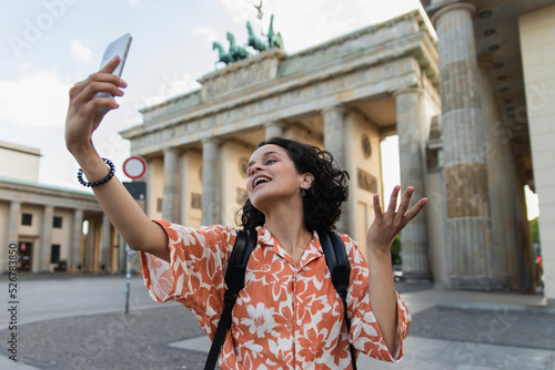 Canvas Print curly tourist with backpack taking selfie on smartphone near brandenburg gate in berlin
