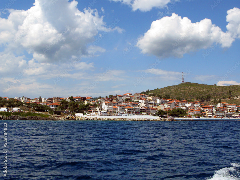 Panoramic photo of coast of small resort town in Greece, blue sea, houses and yachts in distance, beautiful landscape