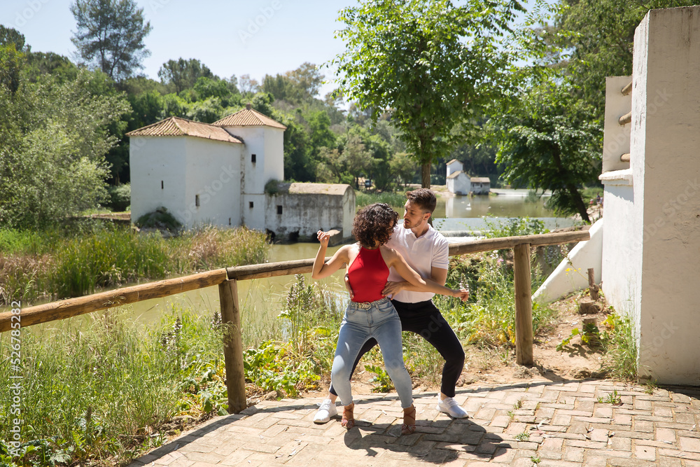 Attractive young couple dancing sensual bachata in an outdoor park with a river in the background. Latin, sensual, folkloric, urban dance concept.