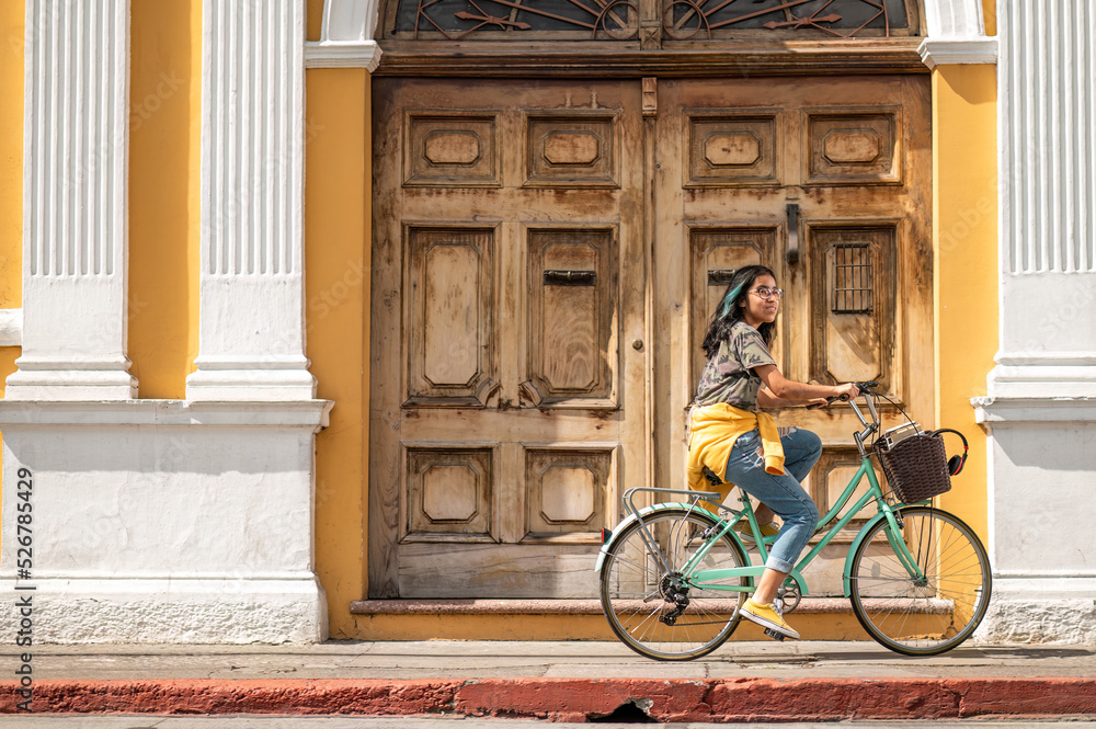 Young woman on a bicycle. Beautiful Hispanic teen riding a bike in front of a colonial house. Young woman on a bicycle. Beautiful Hispanic teen riding a bike in front of a colonial house.