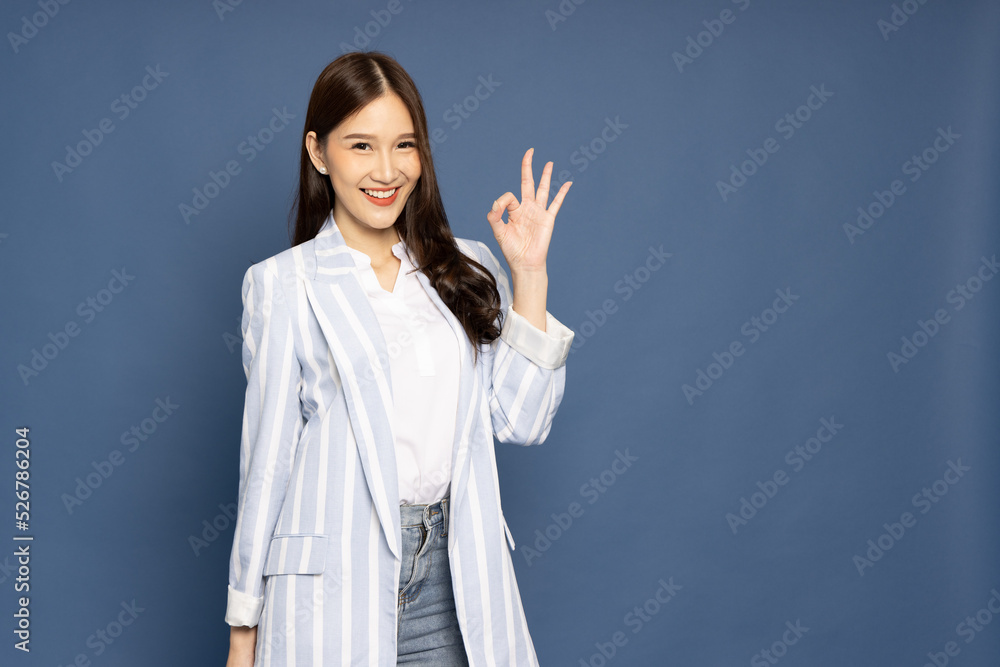 Asian businesswoman smiling and showing OK sign isolated on blue background Asian businesswoman smiling and showing OK sign isolated on blue background