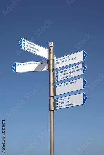 Vertical shot of a post with different signs against a blue sky in Katwijk, Netherlands photo