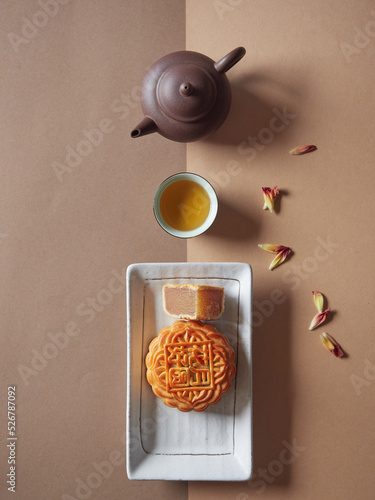 Moon Cake on a plate and a quarter cut showing the stuffing, tea served in cup and teapot. Traditional chinese cake for Mid Autumn Festival. Top view.