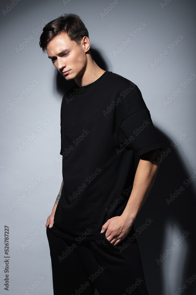 A guy of model appearance in black clothes poses on a gray studio background. Male fashion portrait A guy of model appearance in black clothes poses on a gray studio background. Male fashion portrait